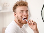 Man smiling while brushing his teeth in bathroom