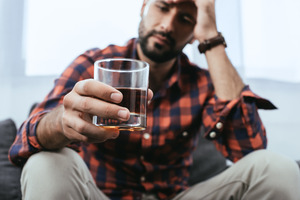 Man holding a glass of whiskey looking concerned